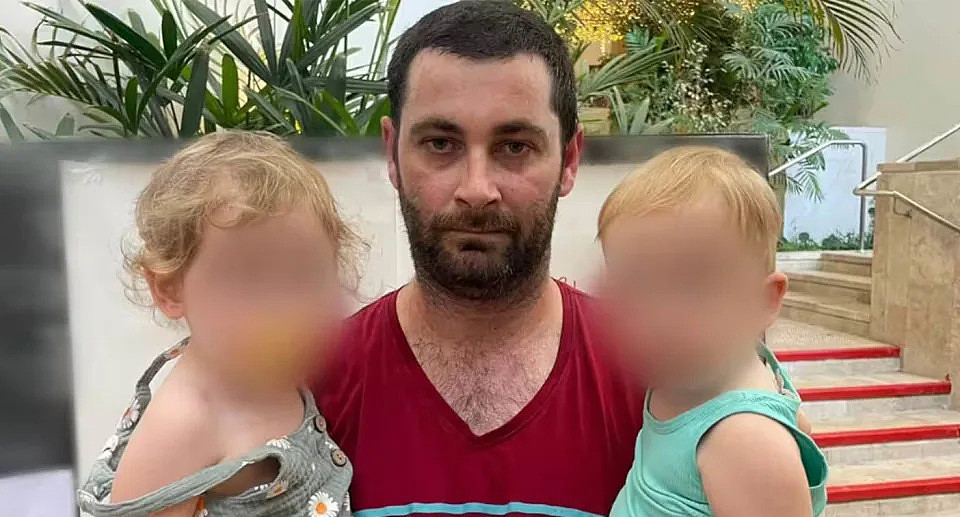 Anthony* holding his two children, who he feared would be captured by Hamas militants. The kids' faces are blurred. 