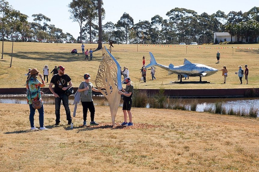 People examine metal sculptures, including one of a shark.