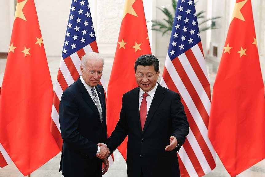 Xi Jinping shakes hands with Joe Biden in front of US and China flags