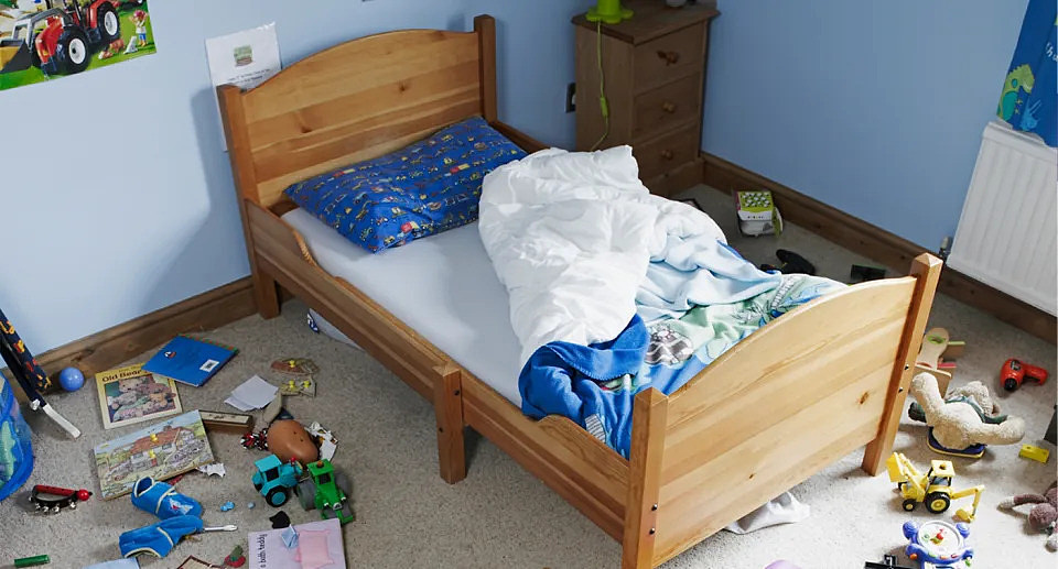 Children's blue bedroom with unmade bed and toys. 