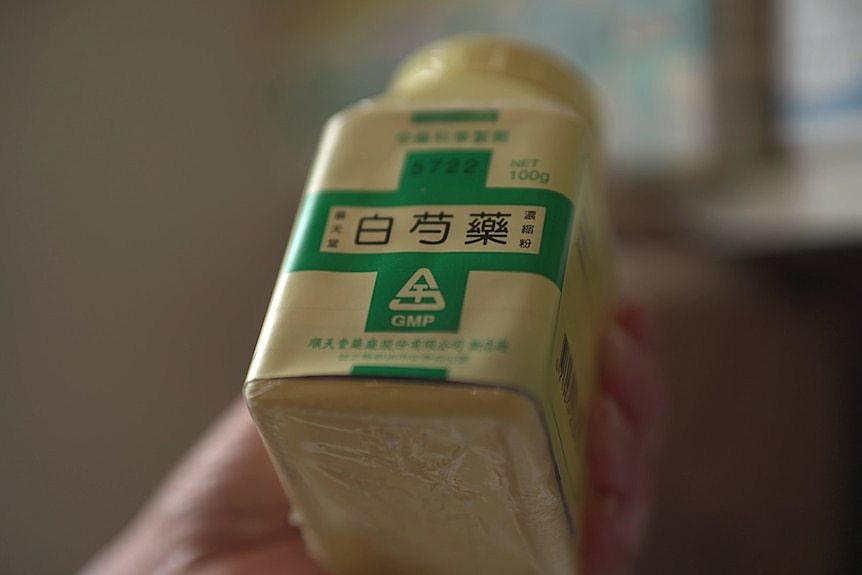 A hand holds up a white bottle of Chinese medicine with green writing.