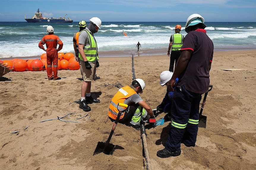 工人们在海滩上埋光缆。