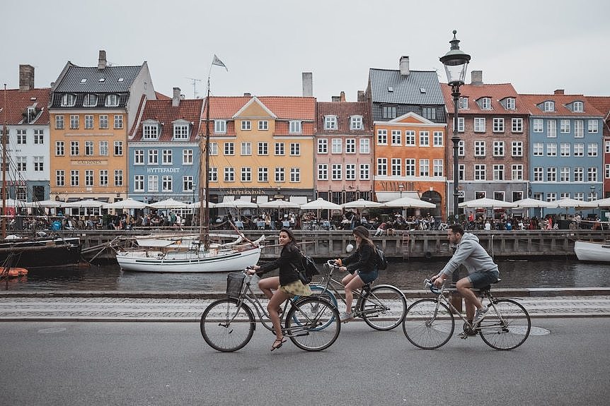 在彩色建筑背景前三个人沿着河骑车。