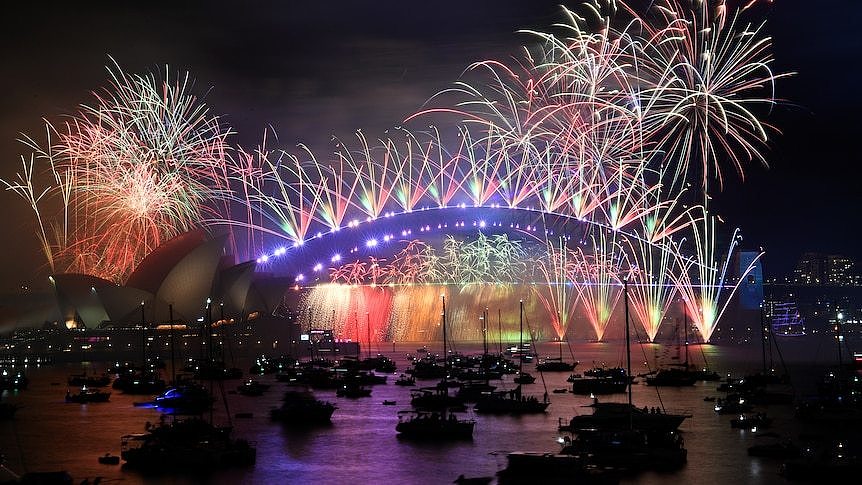 Fireworks light up Sydney Harbour at night. Boats are seen in the foreground.