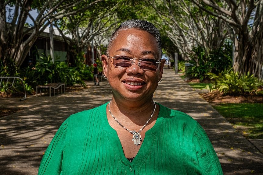 Portrait of a woman wearing sunglasses, standing in an avenue of trees.