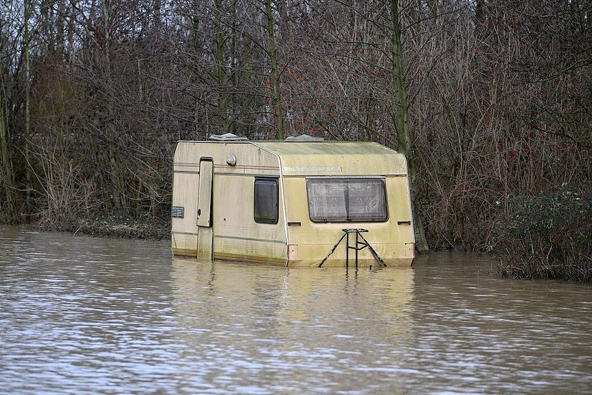 A caravan trailer is submerged under water by flooding near woods in northern France
