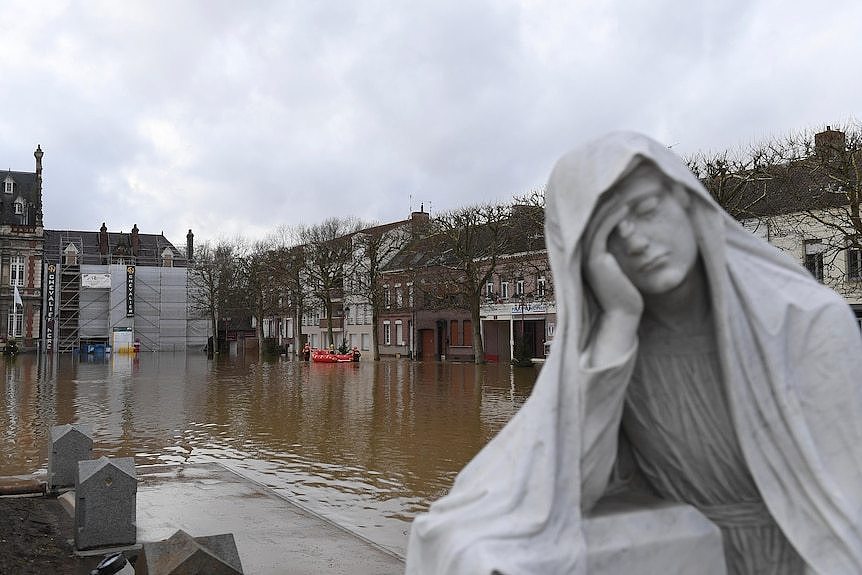 A statue of a woman holding her palm to her face is shown in the foreground of a flooded street in France
