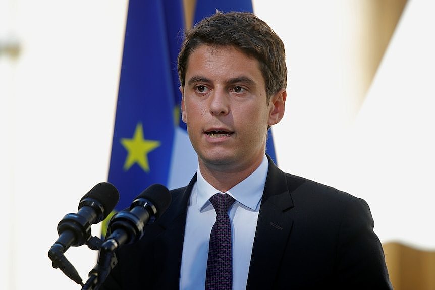 A man in a dark suit speaks at a podium