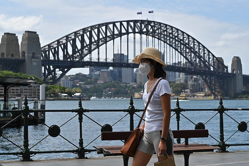 Woman walks past Sydney Harbour Bridge wearing a mask