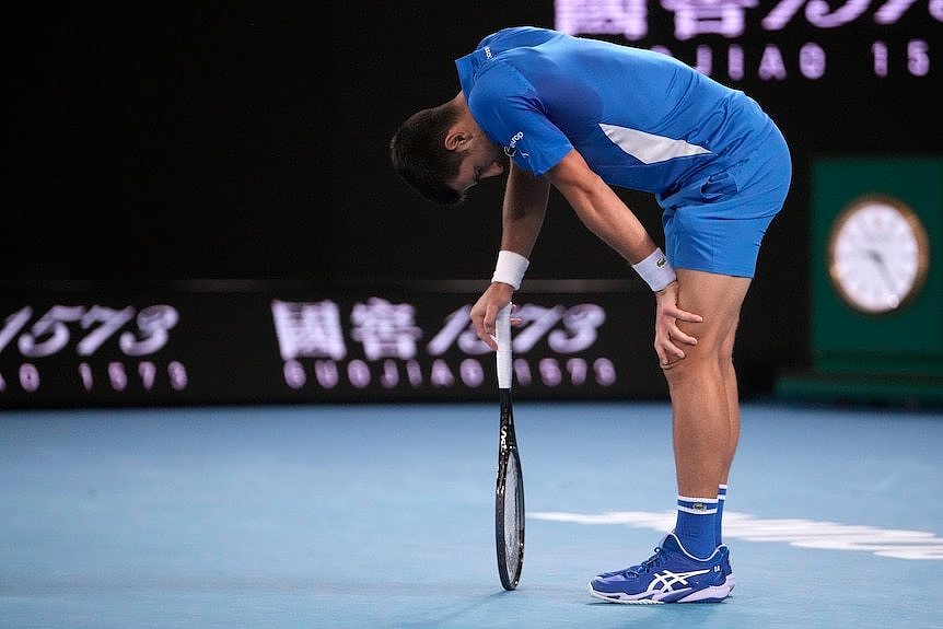Novak Djokovic bends over and leans on his racquet