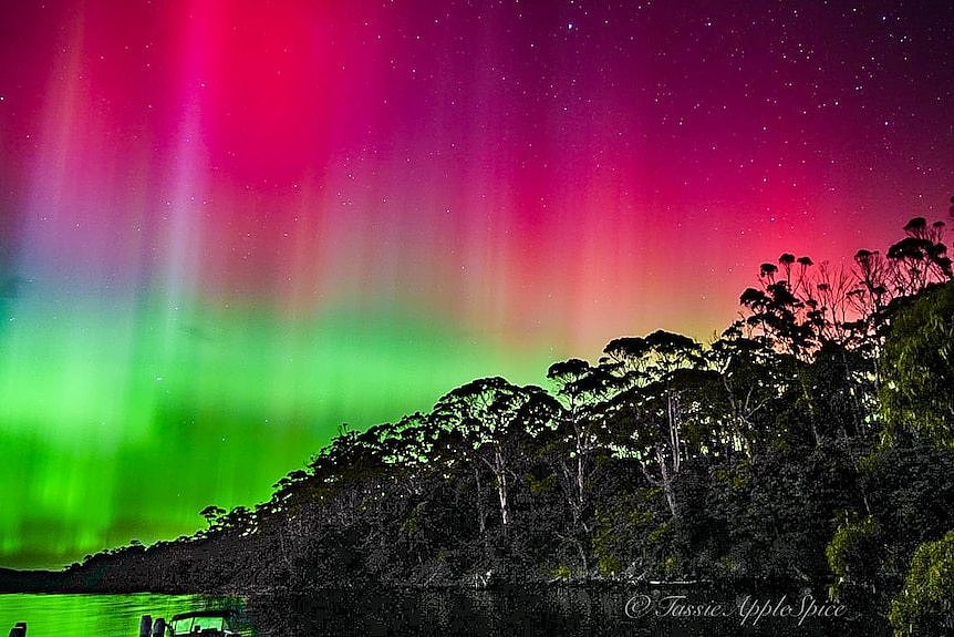 Pink and green lights of an Aurora Australis over water 