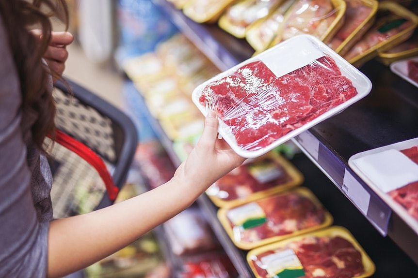A woman holds a tray of meat in a supermarket.
