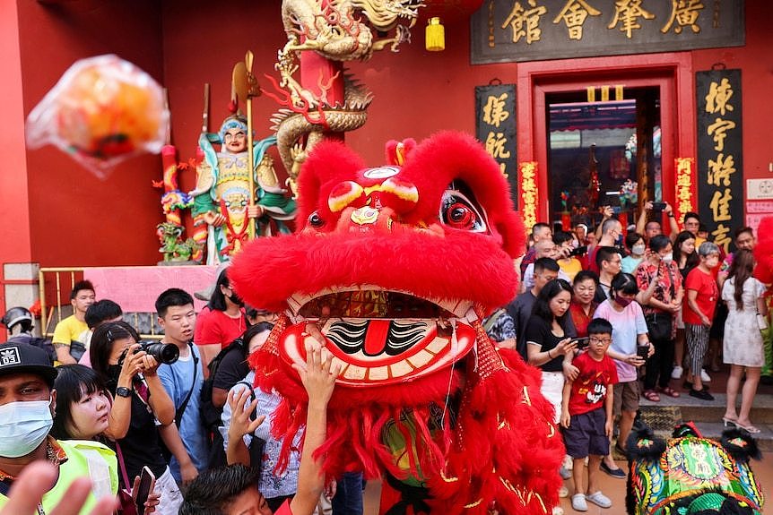 马来西亚吉隆坡，龙年大年初一，信众在关帝庙前观看舞狮表演。