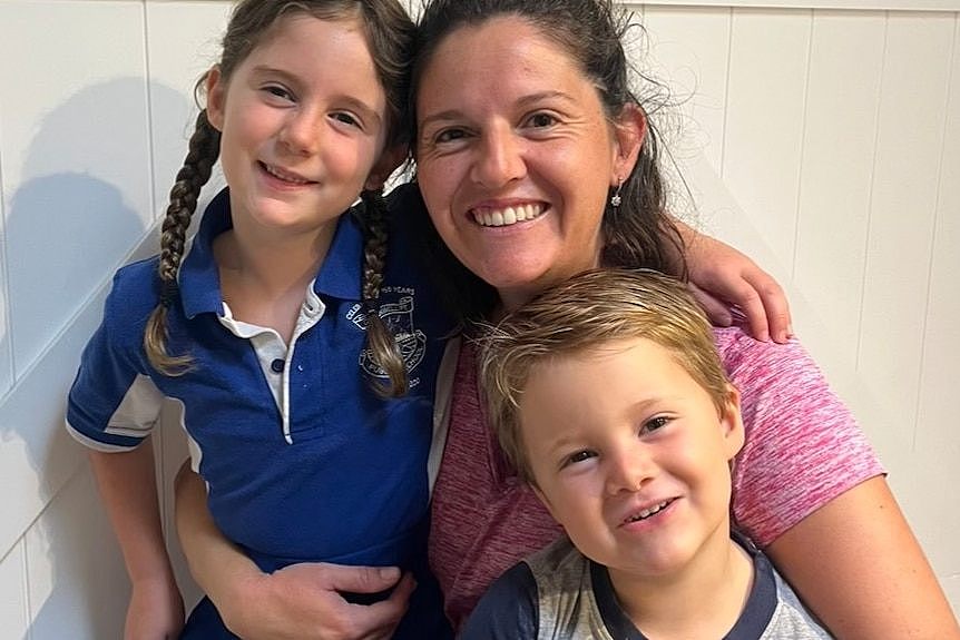 A smiling woman hugs her two young kids.