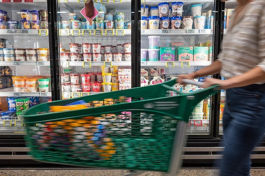A customer wheels a trolley past an aisle of a supermarket with ice cream in freezers.