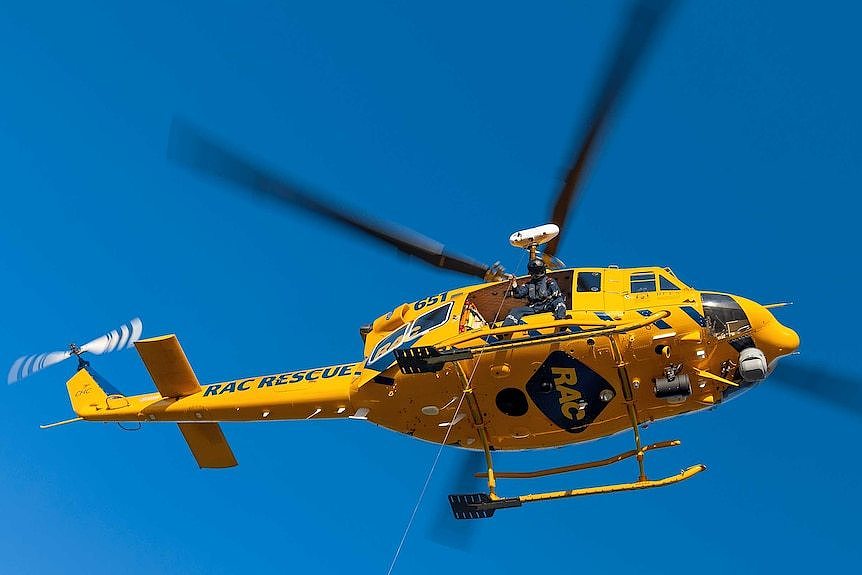 A rescue helicopter hovers in a clear sky.