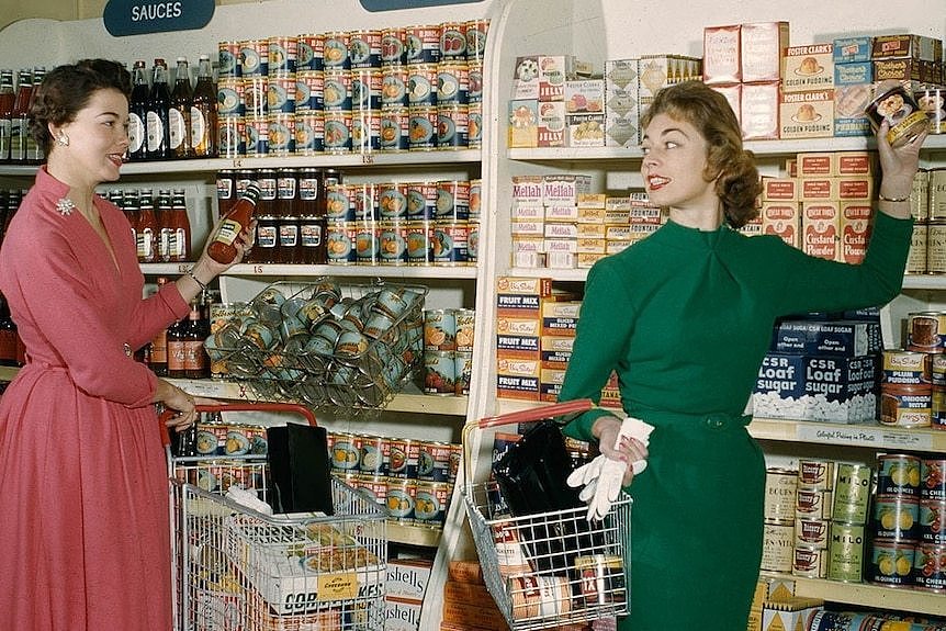 A 1950s photo of two women at a supermarket, taking items off shelves