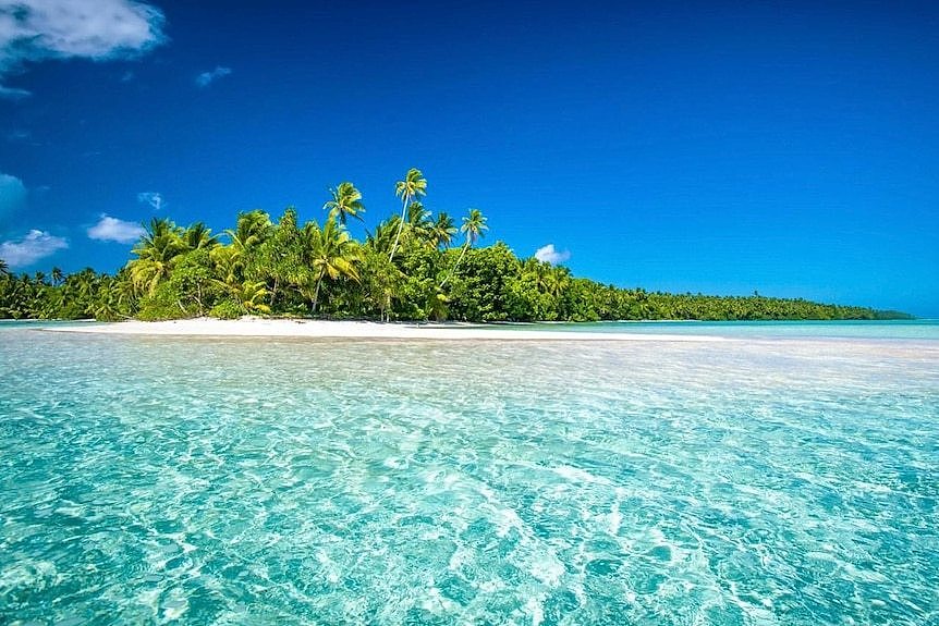 An island with white sandy beaches, turquoise water, swaying palms and blue sky.