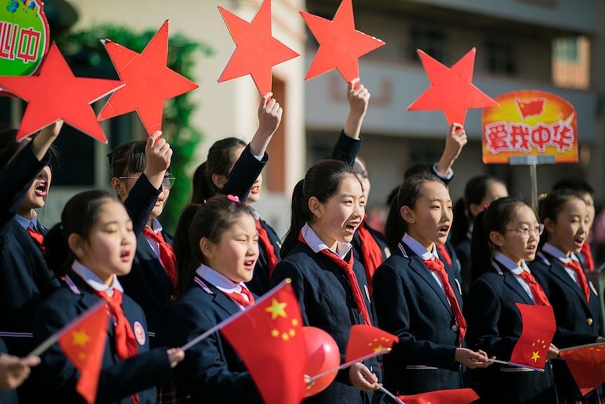 Students hold Chinese flags and cutouts of red stars 