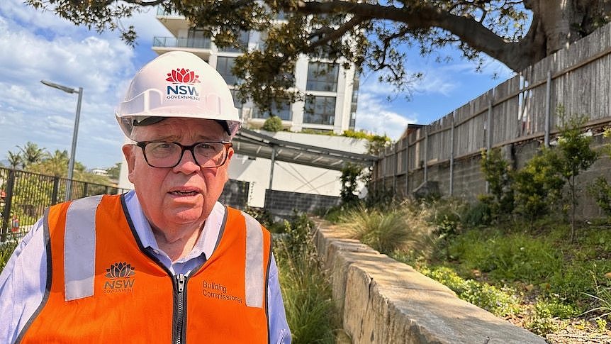 Man wearing a hard hat and high-vis vest standing in front of a building.