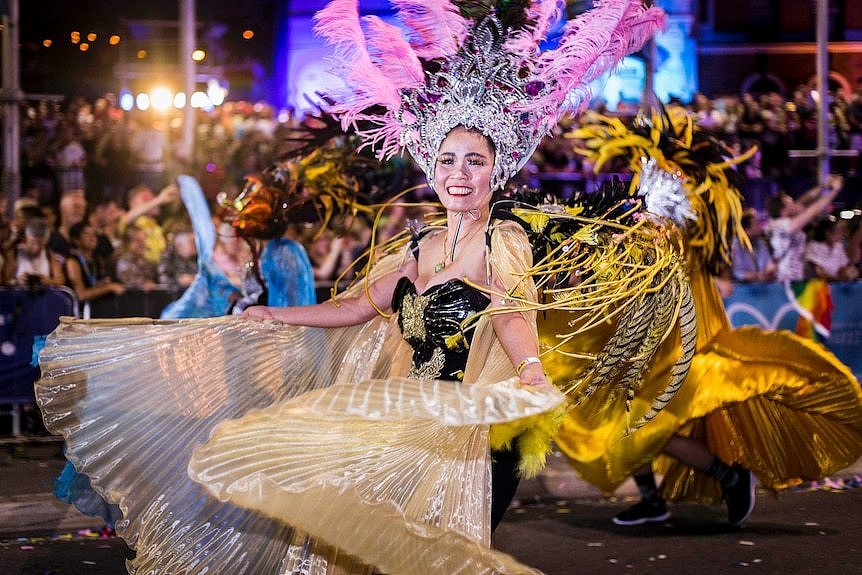 asian woman in feathers twirling a flowing dress in the parade and smiling