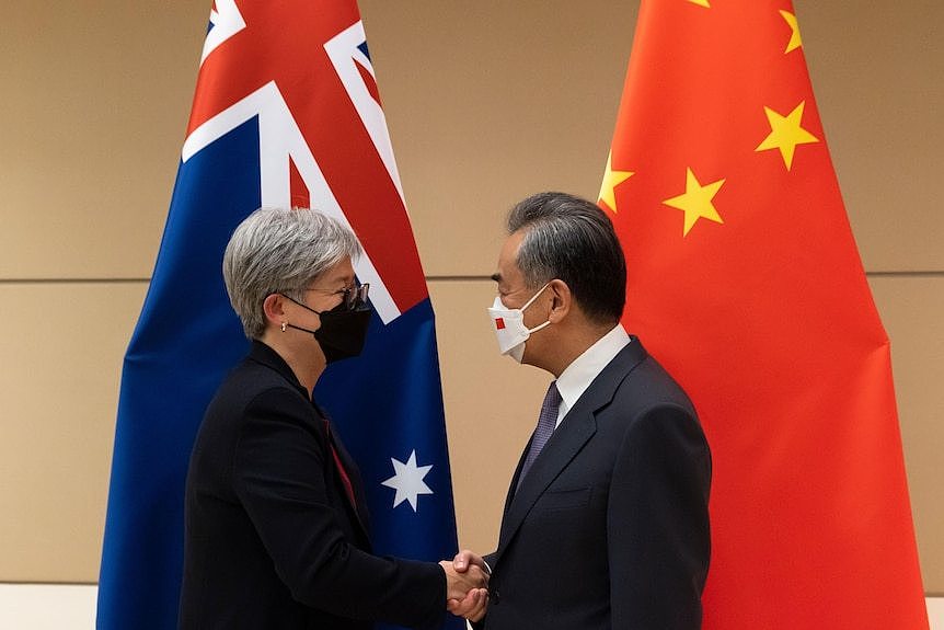 A man and a woman wear face masks as they shake hands in front of the flags of Australia and China.