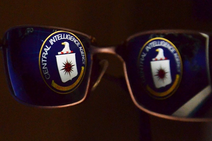 A CIA logo is reflected in glasses.
