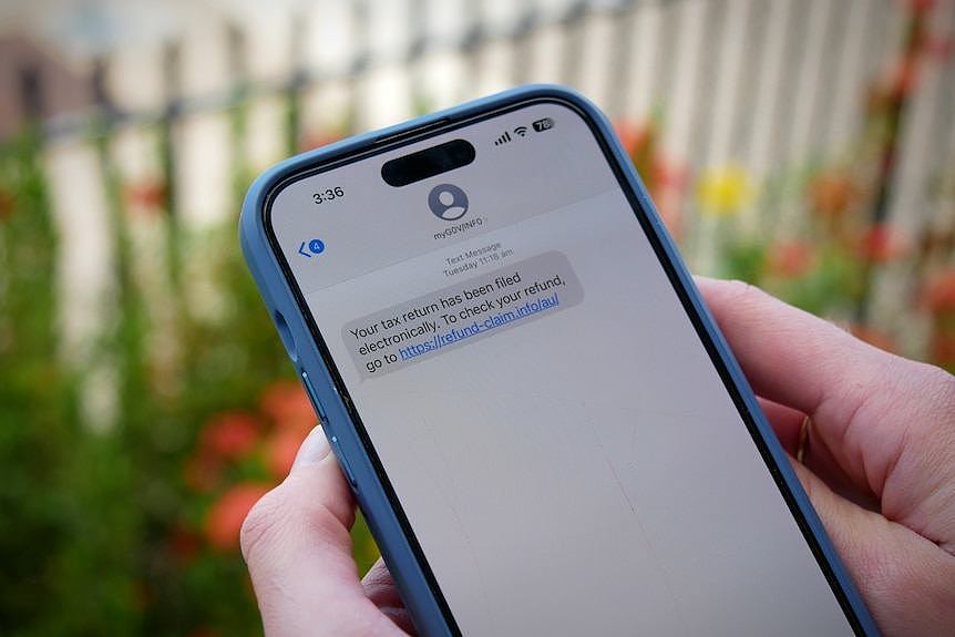 Hands hold a mobile phone displaying a scam text message.