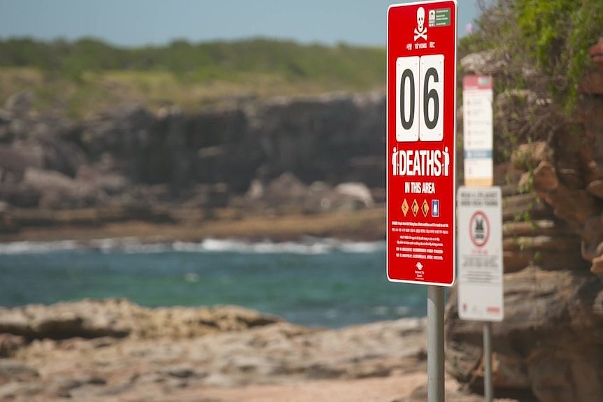 a red sign at a rocky beach with the number 6