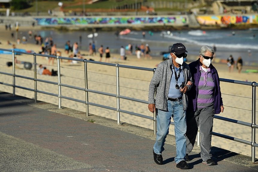 An elderly couple wearing masks walk on the Bondi beach boardwalk.