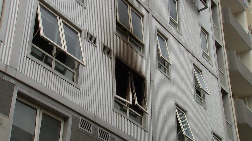 A window on a tall building with black streaks of smoke damage smeared across it.