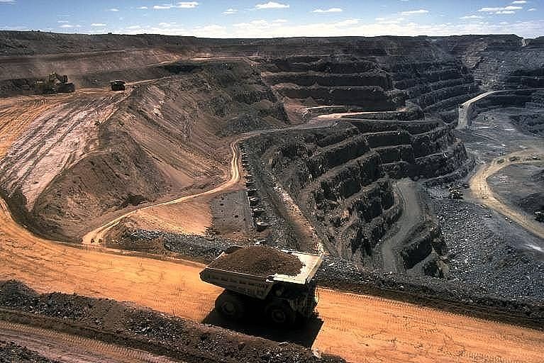 An aerial shot of an open cut coal mine, with a large truck transporting a pile of coal out up a dirt road.