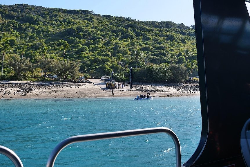 The view from the window of a ferry, looking onto water, sand and a hill.
