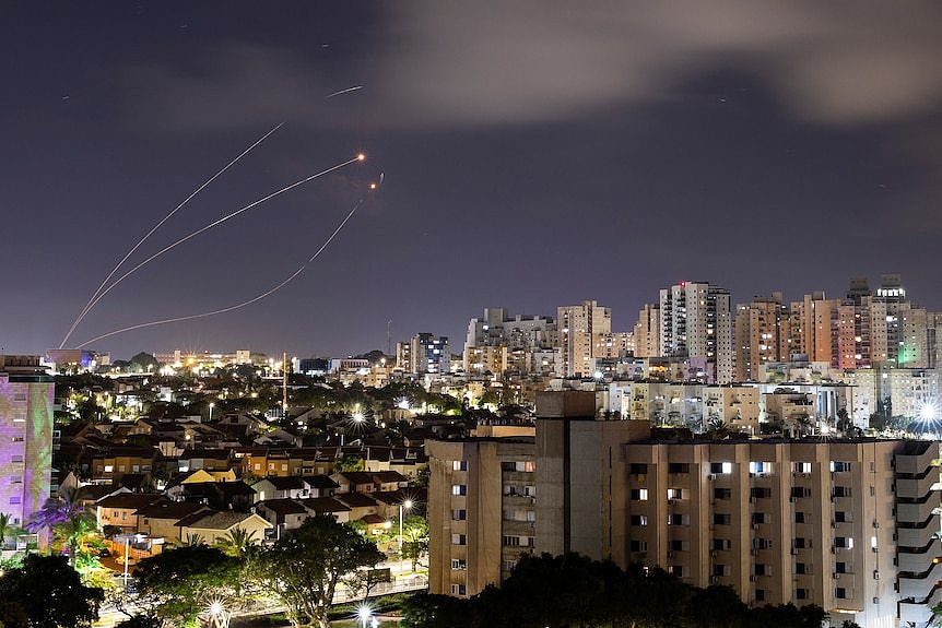 Rocket trails are seen in the night sky over a city skyline.