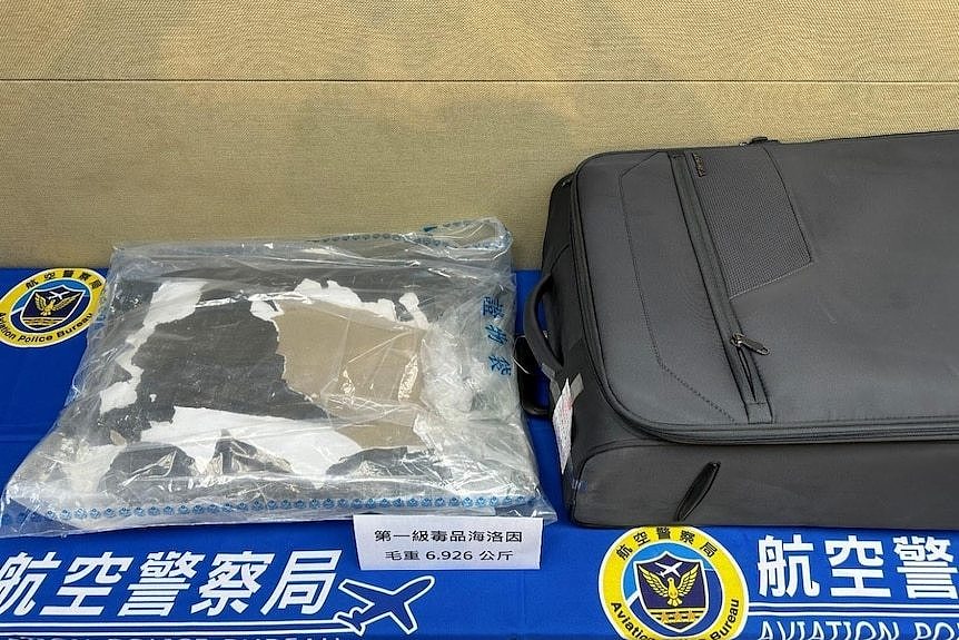 A plastic bag showing torn cardboard lies next to a black suitcase.