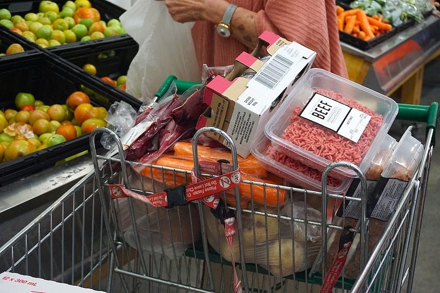 特写镜头：超市里一辆装满杂货的购物车，后面有一位女士正在装袋苹果。