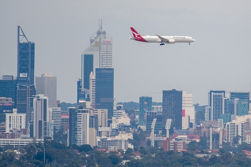 Large white aircraft flying past Perth city skyline