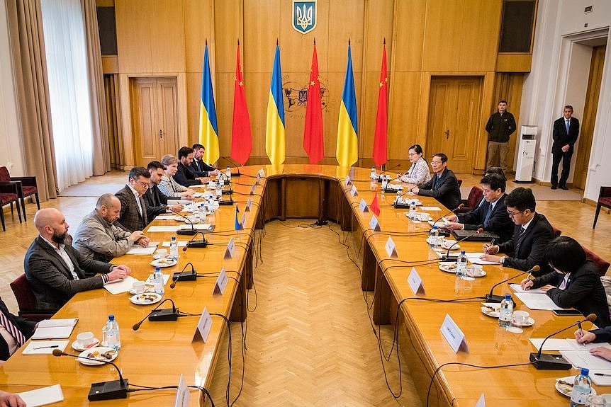 Dignitaries sit at large desk facing each other with Ukrainian and Chinese flags are seen in the background.