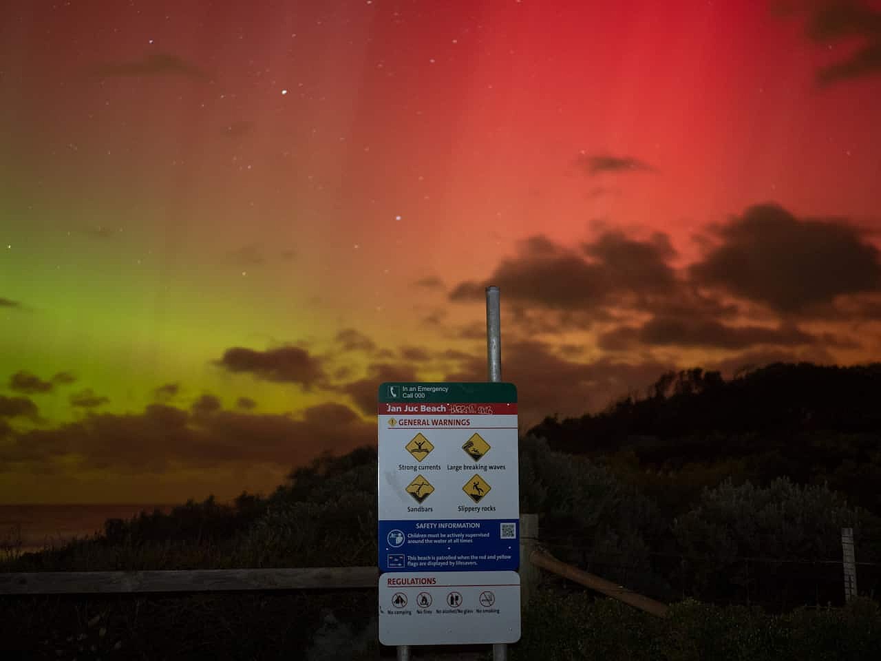 A reddish-yellow aurora australis is seen behind a beach safety sign. 