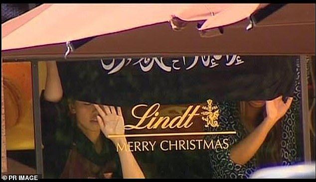 Hostages are pictured holding up a black flag with Islamic writing in the Lindt Cafe in December 2014