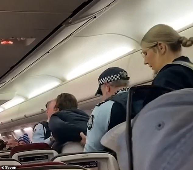 The man was removed from his seat by officers (pictured) after he refused to get up, before he was escorted of the plane as dozens of shocked passengers watched on