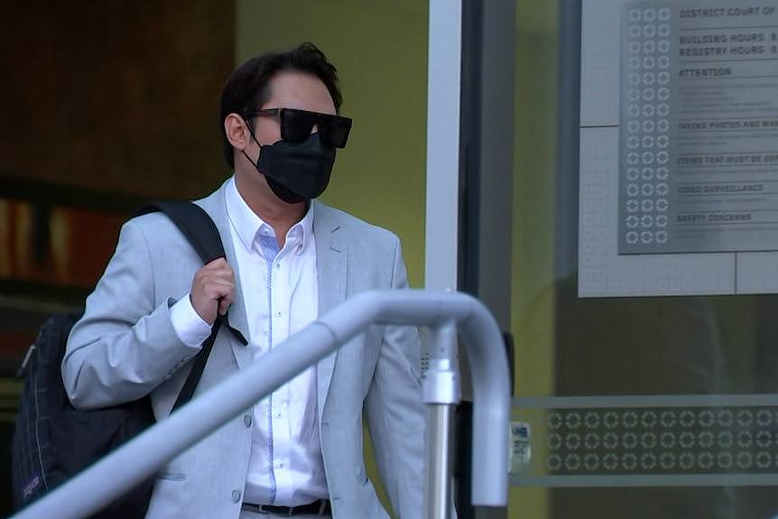 Luke Tham Shengen in a light coloured suit, black mask and glasses, carrying a backpack.
