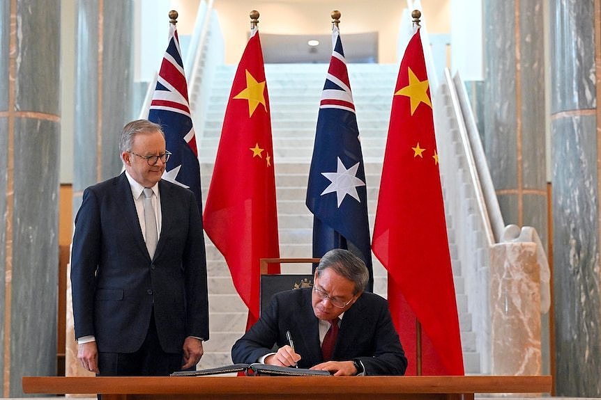 Anthony Albanese watches Li Qiang sign a book in front of Australian and Chinese flags