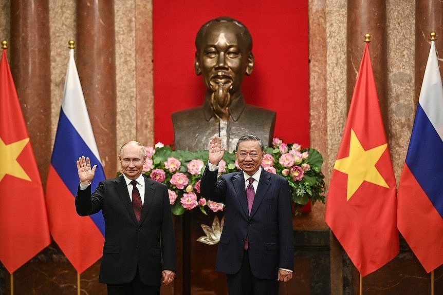 Two men are standing next to each other and each holding one hand up. The flags of Russia and Vietnam are behind them.