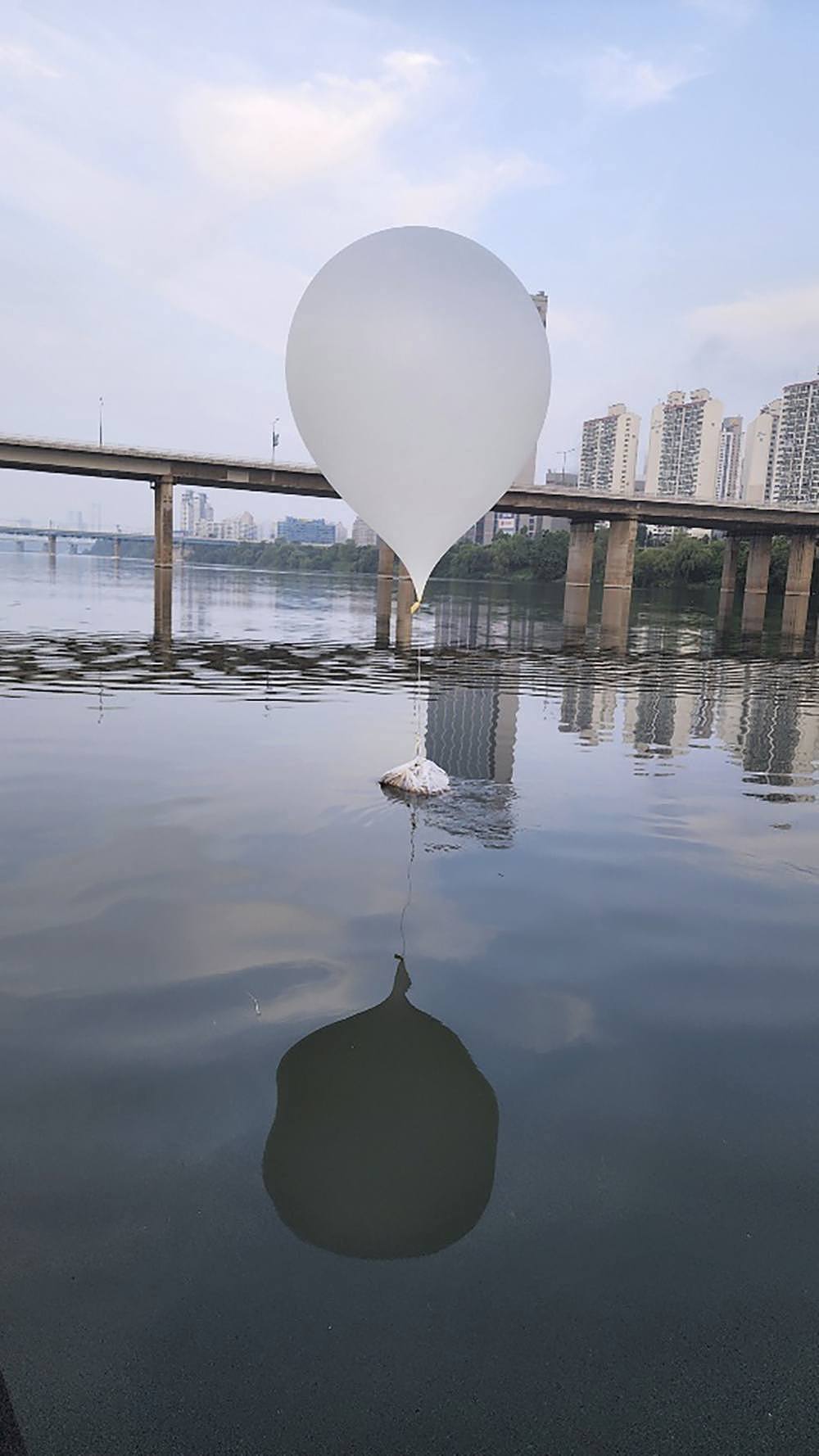 A white balloon attached via to a white bag of trash sits on a river.
