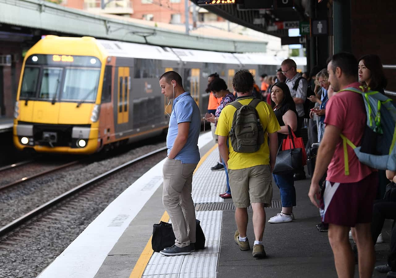 A group of people standing on a train platform. A train on the tracks is behind them.