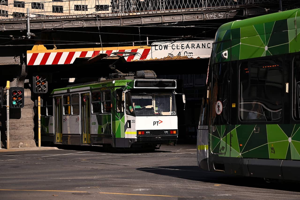 A road with two trams on it. One is going under a bridge.