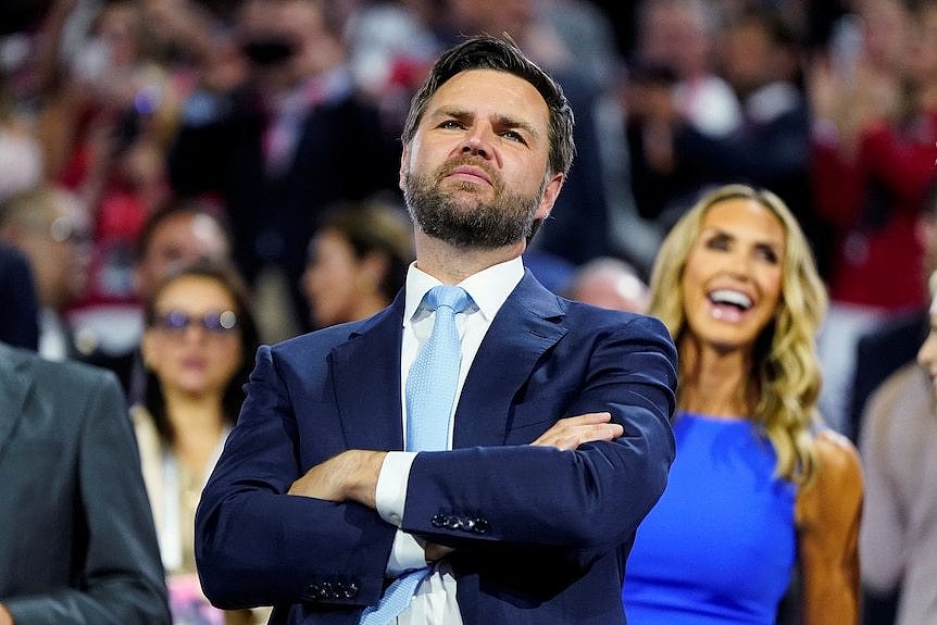 JD Vance stands with arms folded across his chest, chin raised