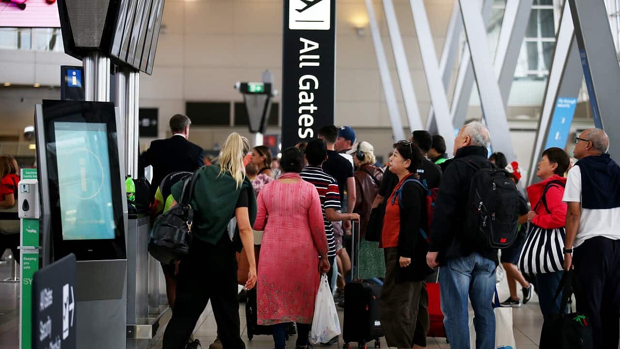 Travellers mill around next to an 'all gates' sign at an airport 