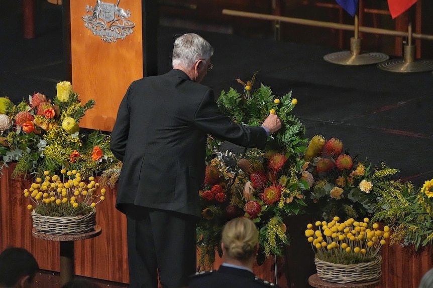 A man holds a small flower, placing it in a wreath inside the great hall of parliament house.